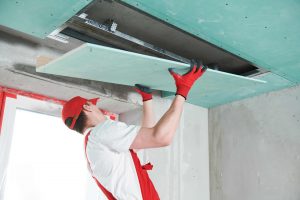 Gyprocker installing a plasterboard sheet in a bulkhead area.