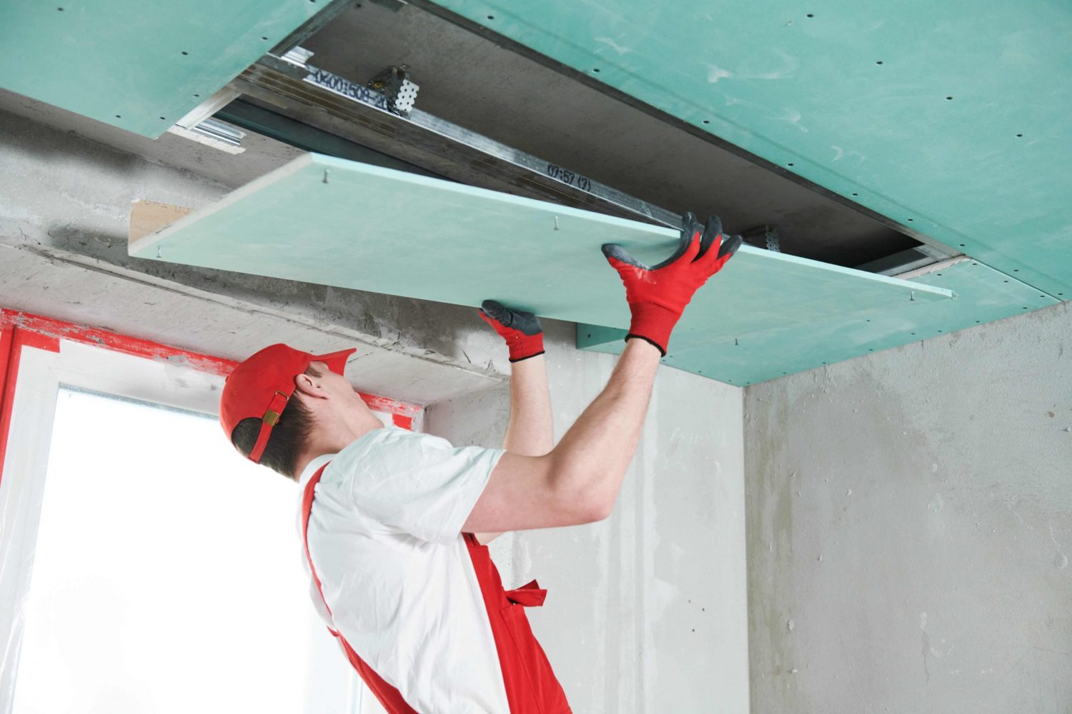 Gyprocker installing a plasterboard sheet in a bulkhead area.