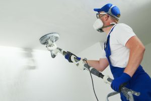 Plasterer sanding ceiling after applying first plaster cover